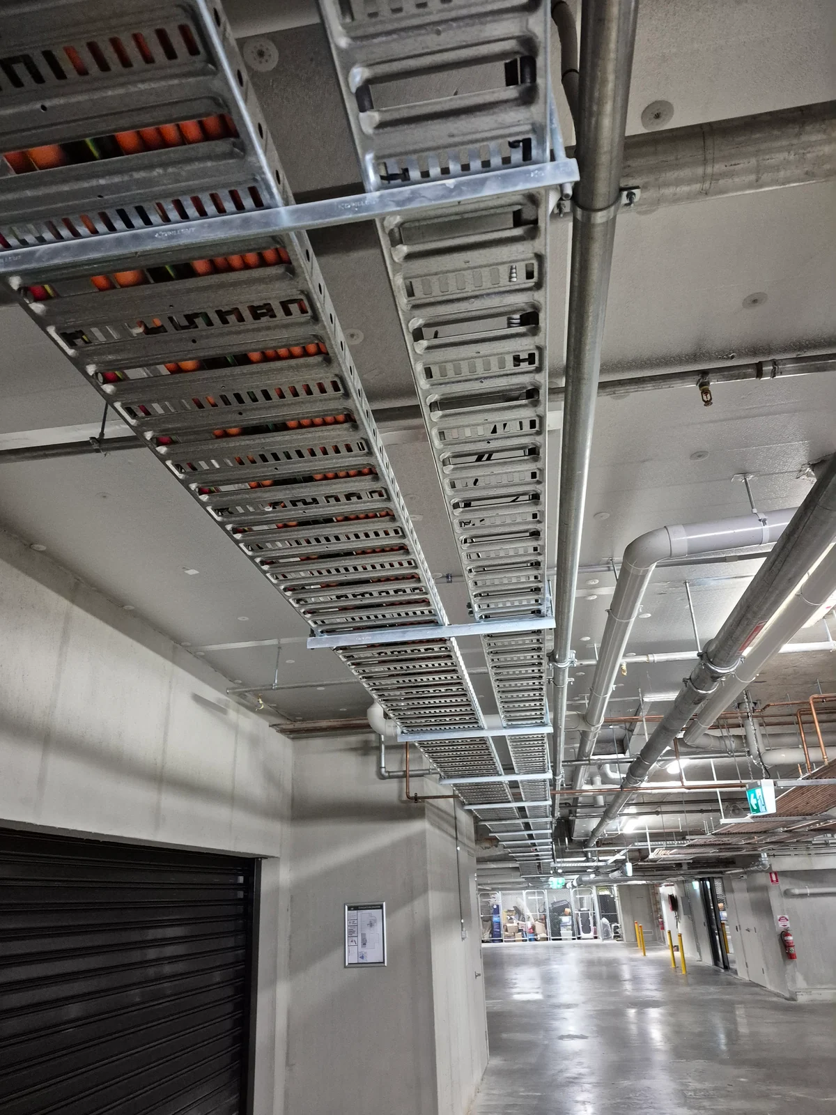 Parallel cable trays and cabling running beneath a concrete ceiling in a service corridor.